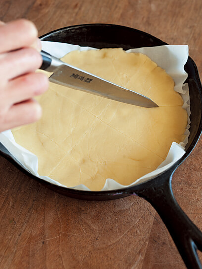 フライパンの上にオーブンシートを敷き詰め、その上に押し付けた生地に、ナイフでうっすらと切り込みを入れる写真：フライパンでらくらくおやつ「ショートブレッド」レシピ／ワタナベマキさん
