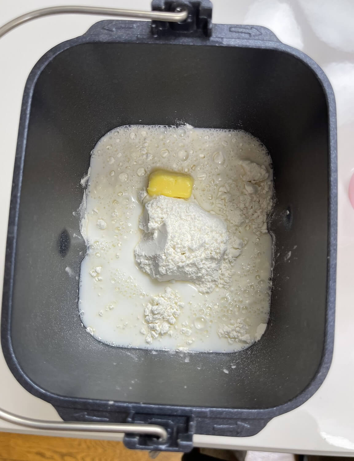 パンケースに強力粉、砂糖、塩、バターを中央を高くして入れたら、水（今回はスキムミルクの代わりに牛乳を使ったので、水＋牛乳）を周囲に回しながら入れます