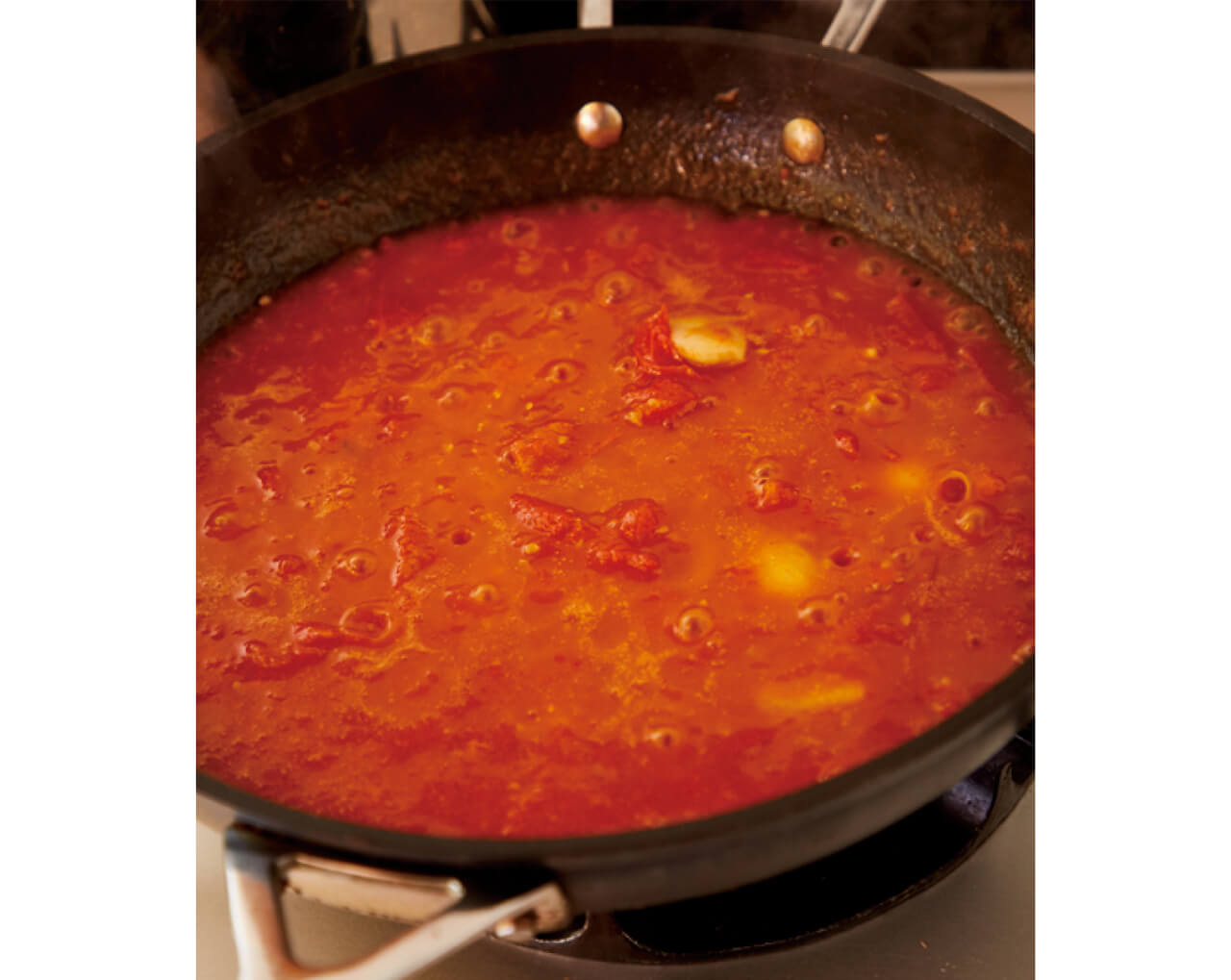 トマトはへらでつぶしながら、フライパンで煮詰める。かたまりが少しだけになって、赤い色がやや黄色みを帯びてきたらOK