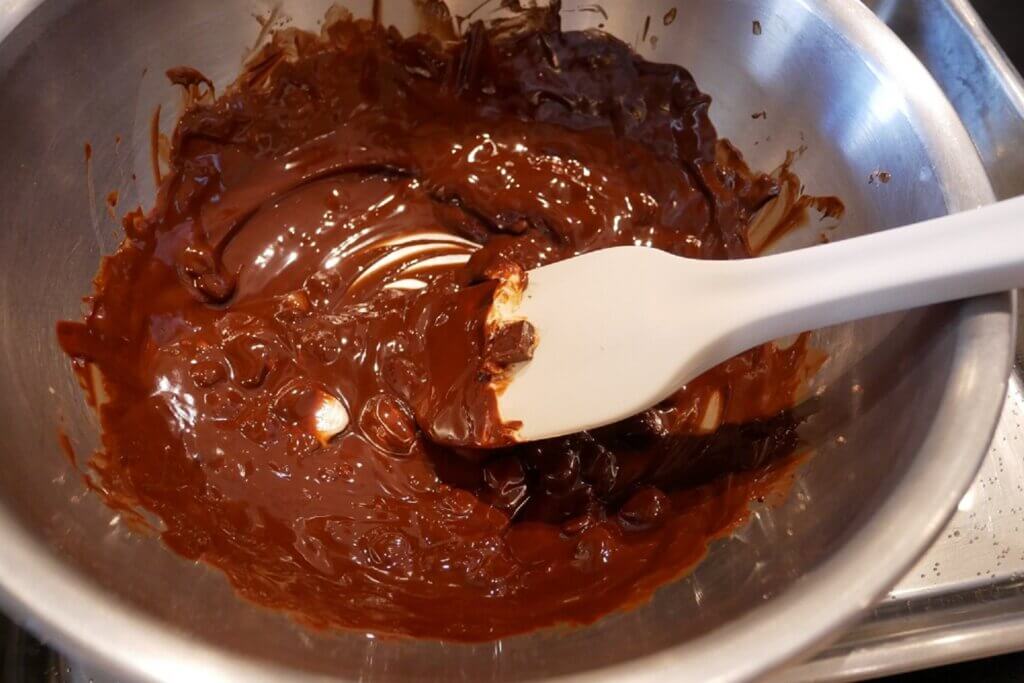 まず、チョコレートとバターを湯煎にかけ、なめらかに溶かして混ぜます。 チョコレートはこまかくカットされているから、すぐに溶けてラク！　