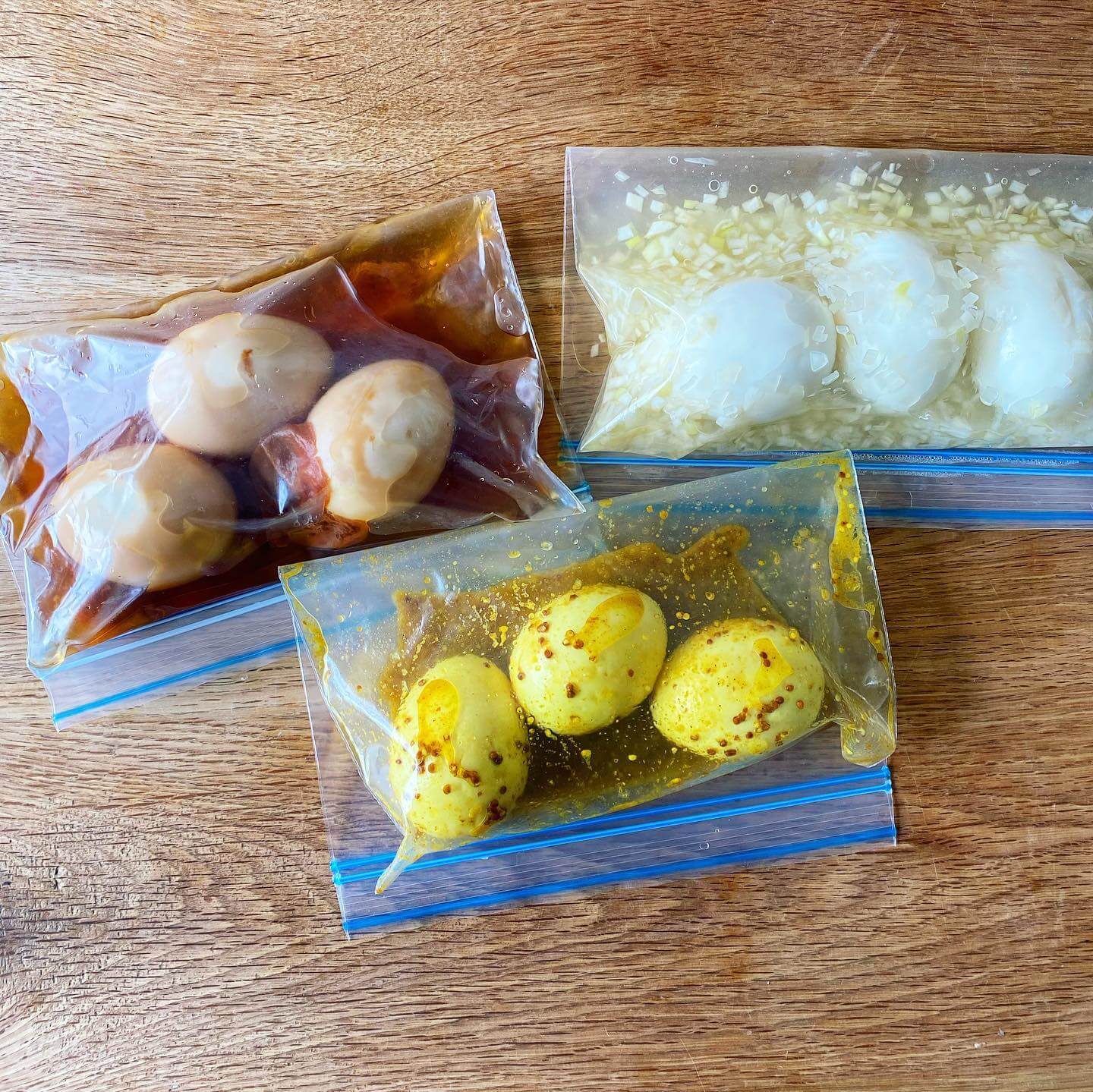 写真：堤 人美さんの「梅めんつゆ味玉」、今井 亮さんの「塩ねぎごま油味玉」、今井真実さんの「ゆで卵のアチャール」、いろんな味玉3種がそれぞれジプロックにつけ汁とともに入っているさま