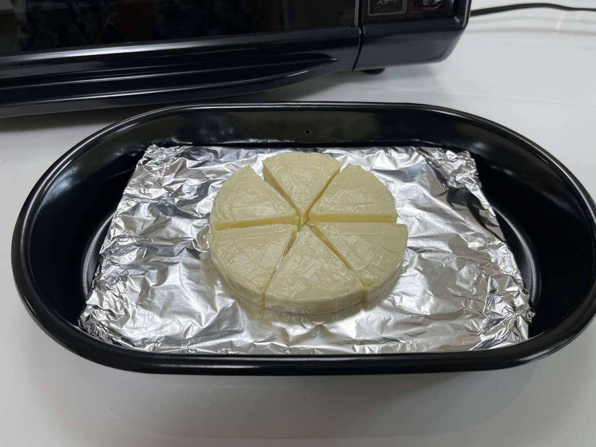 付属のくんせい容器の上にチップ（小さじ3杯）を敷き詰め、くんせい網にアルミホイルを巻き付けてかチーズを置きます