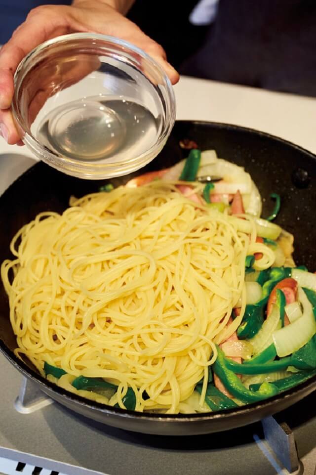 写真：フライパンで炒めた野菜の上にゆで上がったパスタをのせ、ゆで汁をプラスする様子
