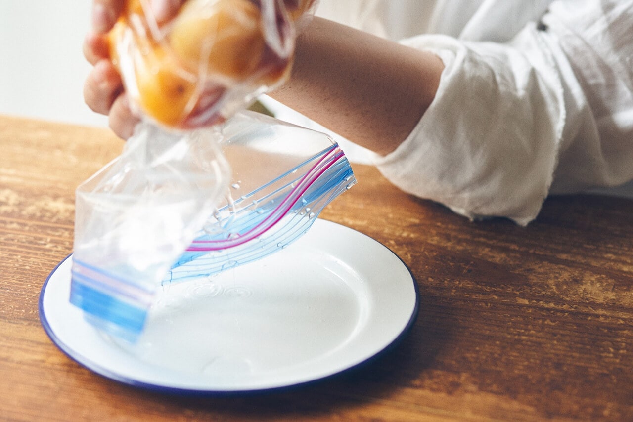 写真：「ジッパー袋で作る梅干し」の工程3-袋から焼酎を白い皿に捨てる様子
