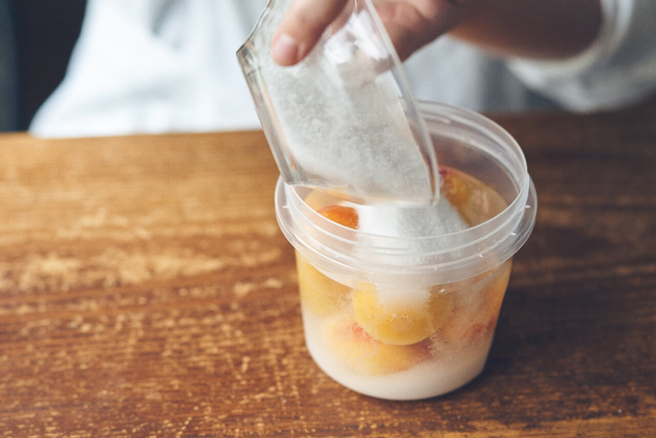 写真：梅と焼酎が入った容器に砂糖を入れる様子