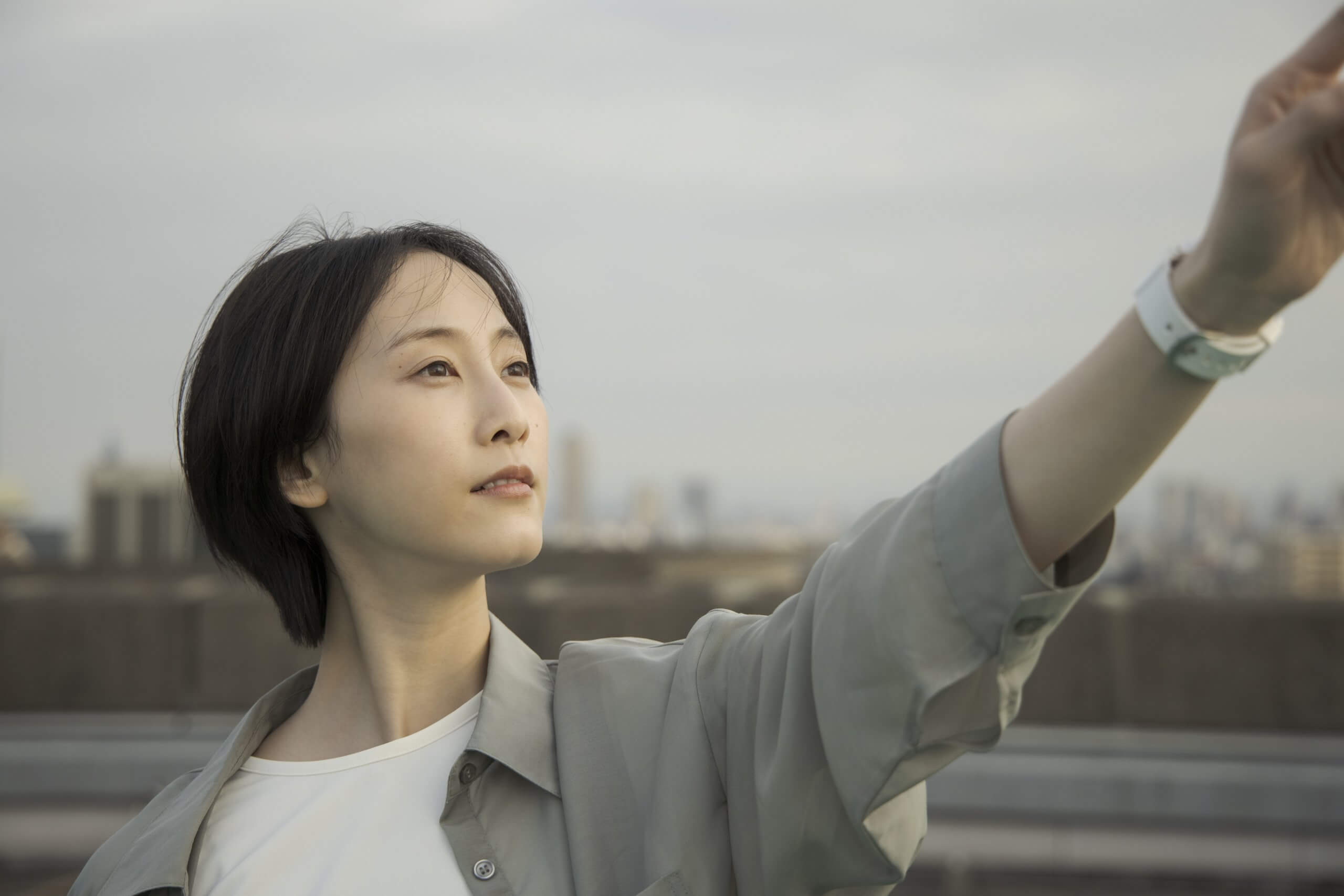 写真：映画作品中の松井玲奈さん。左手を斜め上にかかげ、その方向を見上げる様子