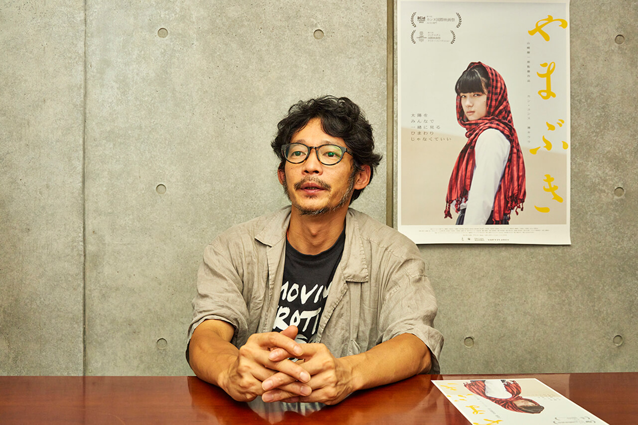 写真：山﨑樹一郎監督と映画「やまぶき」のポスター