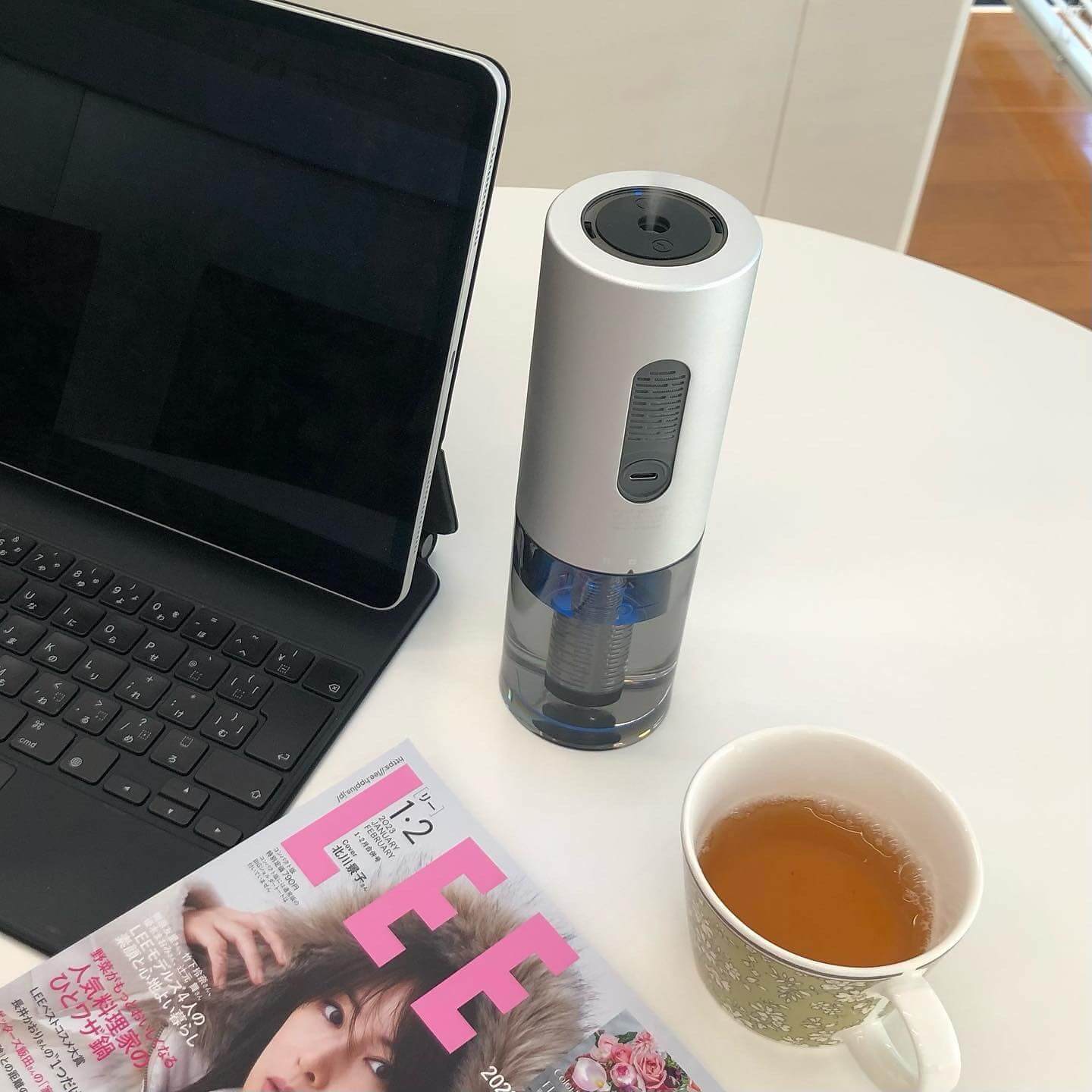 写真：ポータブル加湿器 cado (カドー) STEM Portable（MH－C30）が蒸気を出す様子。PCとお茶と雑誌を載せたテーブルの上で。