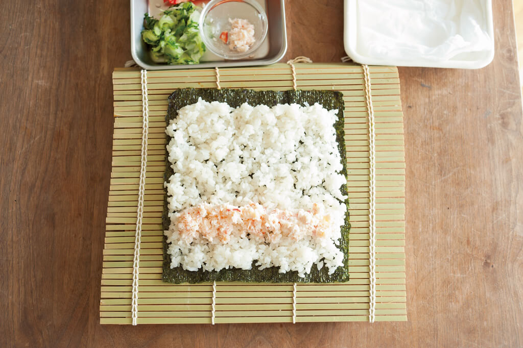 写真：ワタナベマキさんの巻き寿司の巻き方2-1＿ノリにのせたすし飯を広げた上にカニ缶マヨをのせたところ
