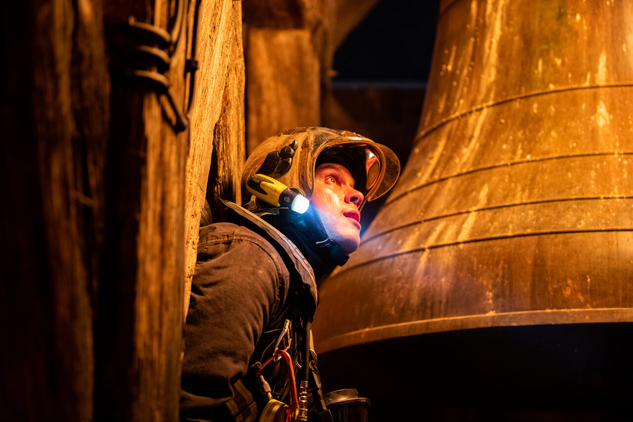 写真：懐中電灯を肩に鐘のそばに立つ消防士