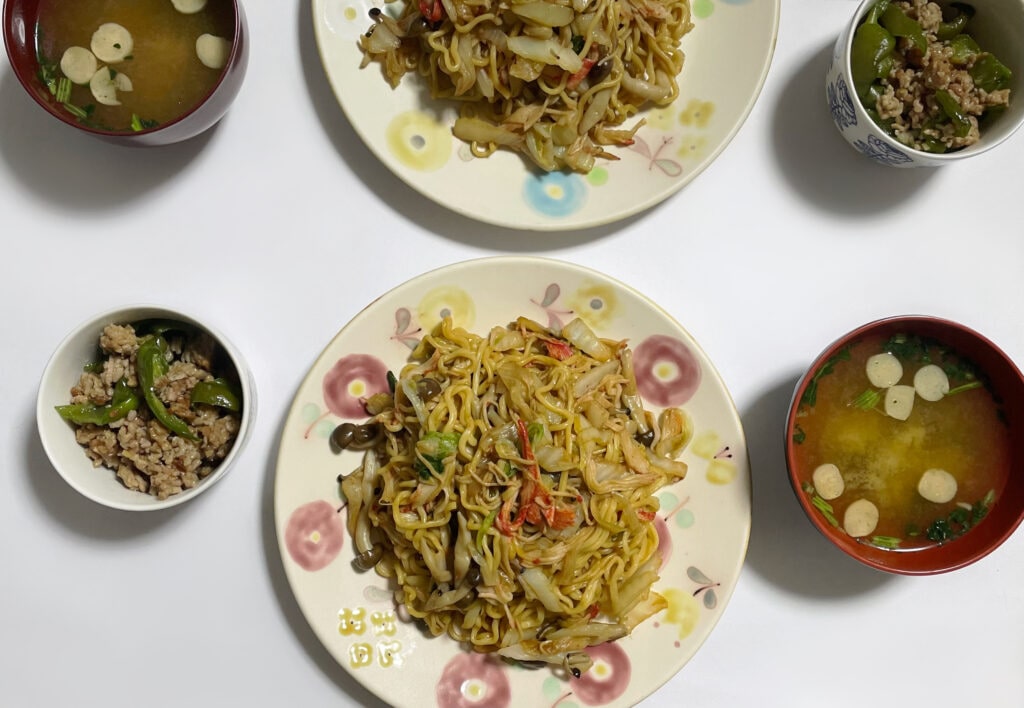 白央篤司さんレシピ「カニかま、青菜、きのこの焼きそば」を40代主婦が作ってみた食卓写真4。森野奈津子さん作陶の花柄のプレートに盛り付けされ、ピーマンとひき肉の炒め物やお麩とほうれん草のお味噌汁が並んだ食卓。