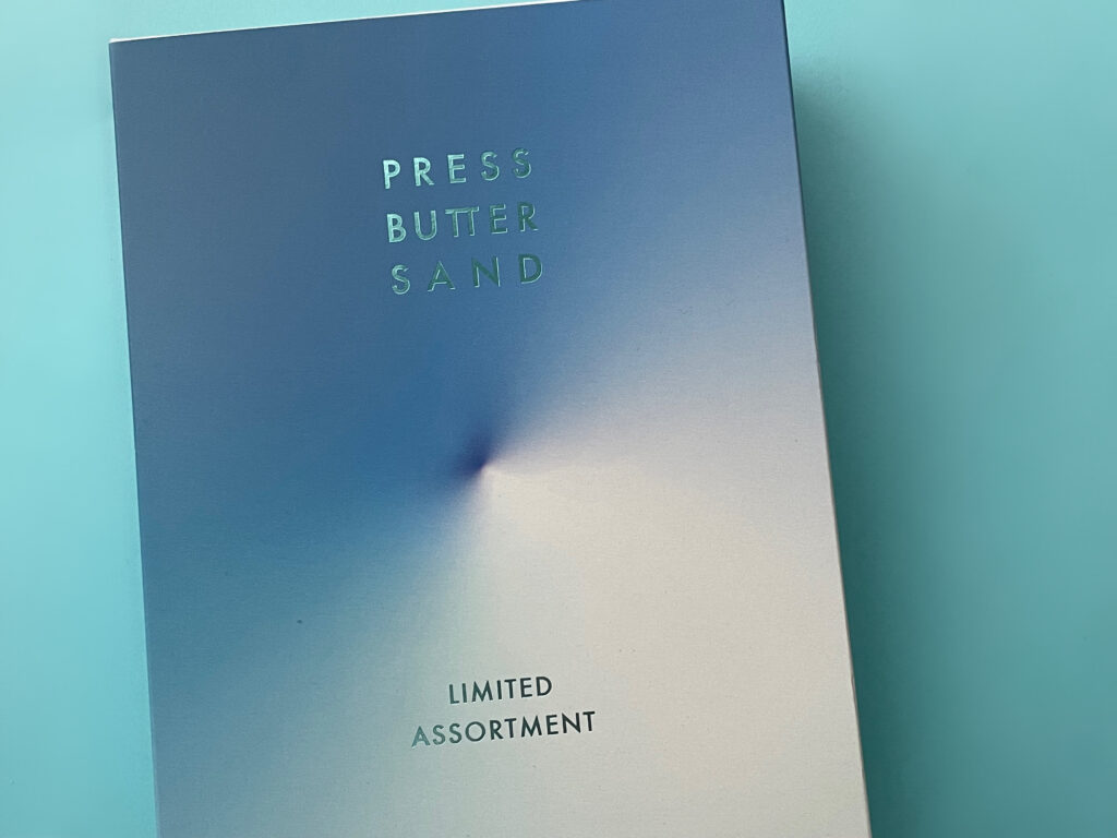 から白へのグラデーションが美しい、PRESS BUTTER SANDの「LIMITED ASSORTMENT」限定アソートパッケージ。背景は無地のライトブルー。