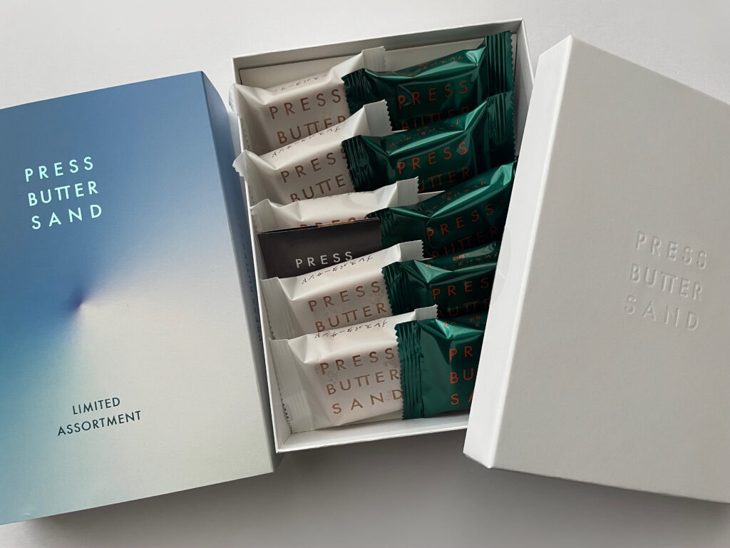 羽田空港限定パッケージに入ったPRESS BUTTER SANDのプレーンと珈琲の詰め合わせ。白と緑の個包装が整然と並ぶギフトボックスの写真