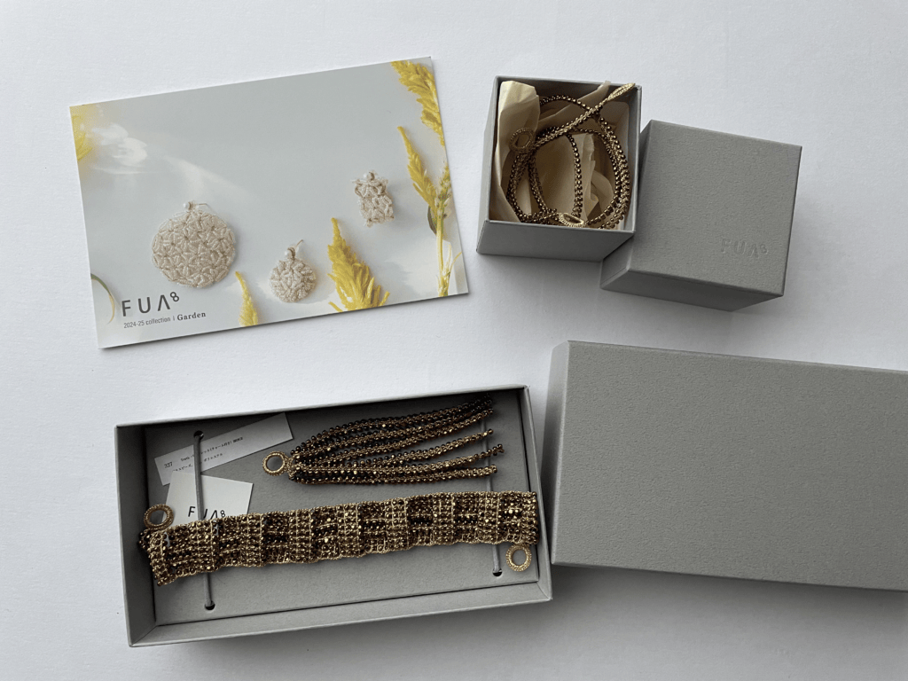 FUA accessoryのロゴ入りグレーの箱を開けた状態。中にはブレスレットとネックレスが収納されており、ブランドカードも添えられている。