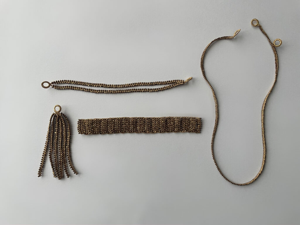 FUA accessoryのtruthシリーズ。ブレスレットのチェーン、タッセル、編み込みパーツ、連結チェーンの3パーツと、シンプルなゴールドネックレスを平置きで並べて撮影。
