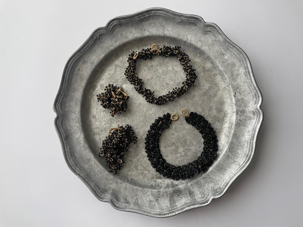 FUA accessoryの「はじまりの時」と「garden」シリーズのハンドメイドアクセサリー。黒ビーズを用いたブレスレットとイヤリングが、ヴィンテージ調のシルバートレイの上に平置きされた商品撮影。