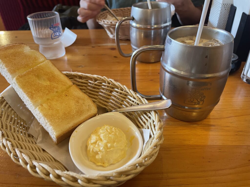 コメダ珈琲店のモーニングサービス。たっぷりサイズのアイスミルクコーヒーと山食パンにマーガリン、手作りたまごペーストの写真。食パンはかごに盛付けされている。