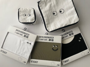 LEE100人隊TBはなが発売日に購入した、ユニクロ×アニヤ・ハインドマーチのコラボ2025を5点並べた写真。スクエアポーチのLARGEとSMALLが1点ずつ、KIDSのクルーネックTはGREENとWHITE、ボクシーTはBLACKのMサイズが各1点ずつ。Tシャツのパッケージには“ANYA HINDMARCH T-SHIRT SHOP”の文字が入っている。アニヤ・ハインドマーチのアイコン的存在“eyes”のデザインが印象的。