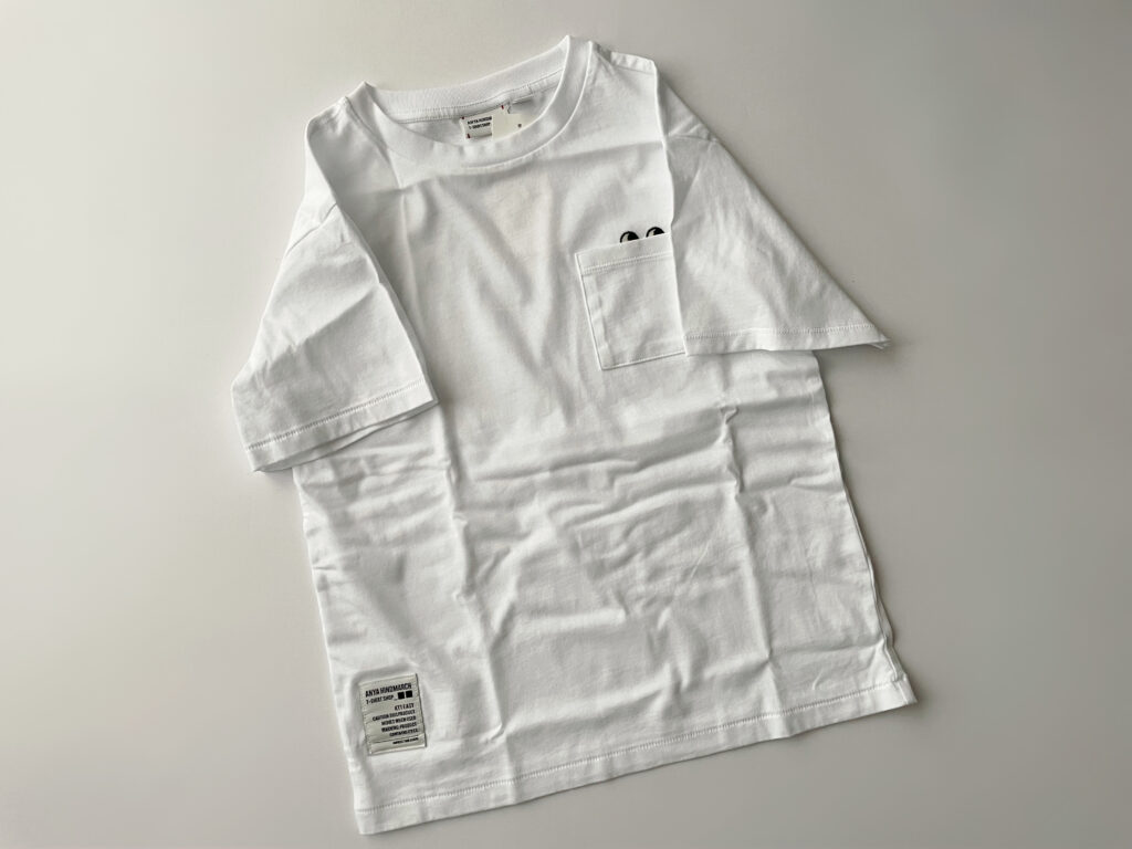 ユニクロ×アニヤ・ハインドマーチのコラボのTシャツ、KT1EASY/クルーネックTのWHITE。サイズは130cm。胸ポケットからはEyesが覗いている。左右それぞれの袖に異なるステッチが施され、右前裾にはデザインラベルが貼付してある。