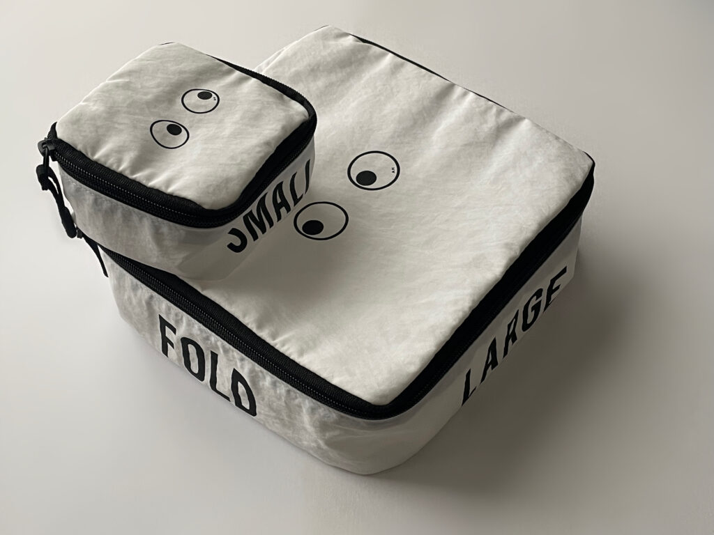 ユニクロ×アニヤ・ハインドマーチのコラボ、スクエアポーチとミニスクエアポーチを2段に重ねた写真。ミニスクエアポーチにはサイドに“SMALL”、スクエアポーチのサイドには“FOLD”・“LARGE”のロゴが入っており、eyesのデザインがユニーク。