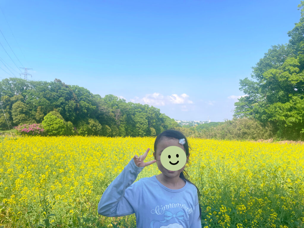 スタンプで顔が隠された女の子の背景には青空と菜の花畑が広がっている。