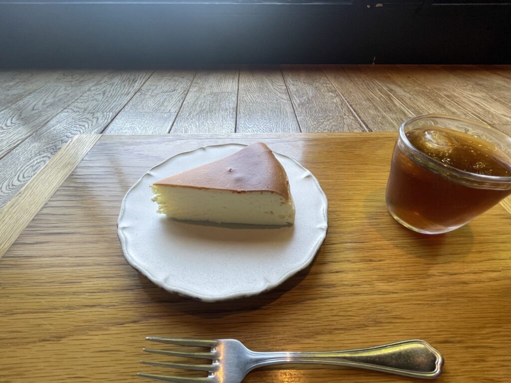 JIKE STUDIOのチーズケーキ、寄りの写真。石岡信之さん作陶のケーキ皿に盛り付けされている。右には冷たいお茶。