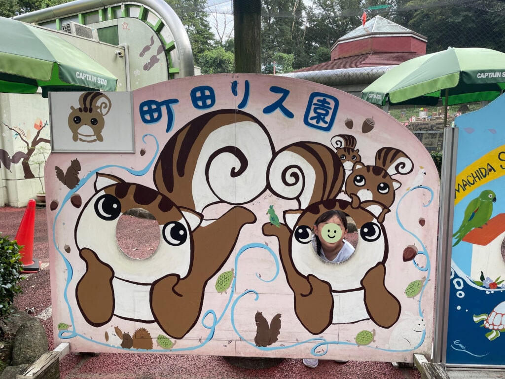 町田リス園の顔はめパネル。背景がピンク、可愛いリスが頬杖をついているイラスト。