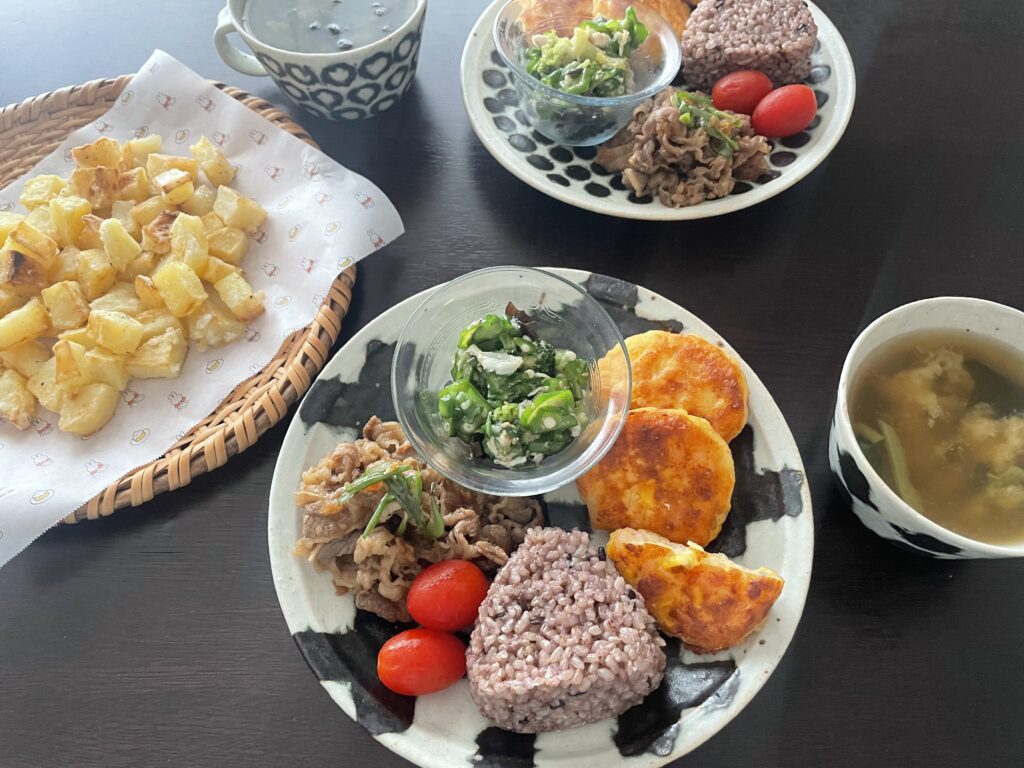 結わえる×セブンイレブンのコラボの「寝かせ玄米®おむすび」がのったワンプレートランチ。海老とトウモロコシのさつま揚げや牛肉の焼き肉、ミニトマト、オクラとサラダチキンの和え物などがのっている。