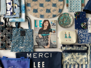 LEE7月号（2025年）と、ブルー特集にリンクさせた青い小物集め。ミナペルホネンのpartyやrosasのバッグ、ミナペルホネンの手ぬぐいやLEE40周年イベントのエコバッグ、Tartineの双子姉妹柄のポーチやGUのネックレス・ブレスレット、オールドマンズテーラー（R＆D.M.Co-）のブルーストライプのエコバッグなどが並んでいる。