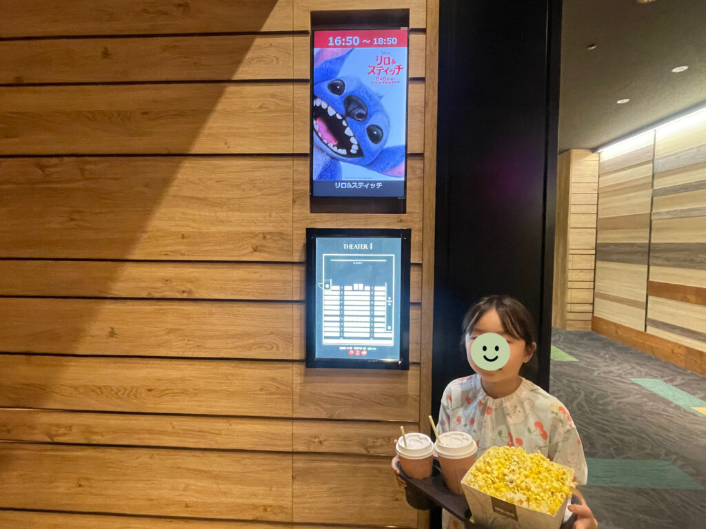 実写映画『リロ＆スティッチ』のシアター入口でポップコーンを持っている小学生女児。