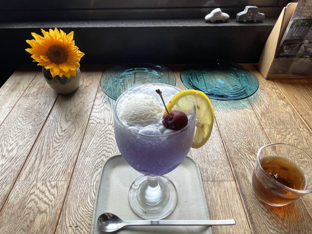 JIKE STUDIOカフェの青いクリームソーダ。天然色のオーガブルーソーダと自家製ミルクジェラート。ひまわりの花が飾られている。