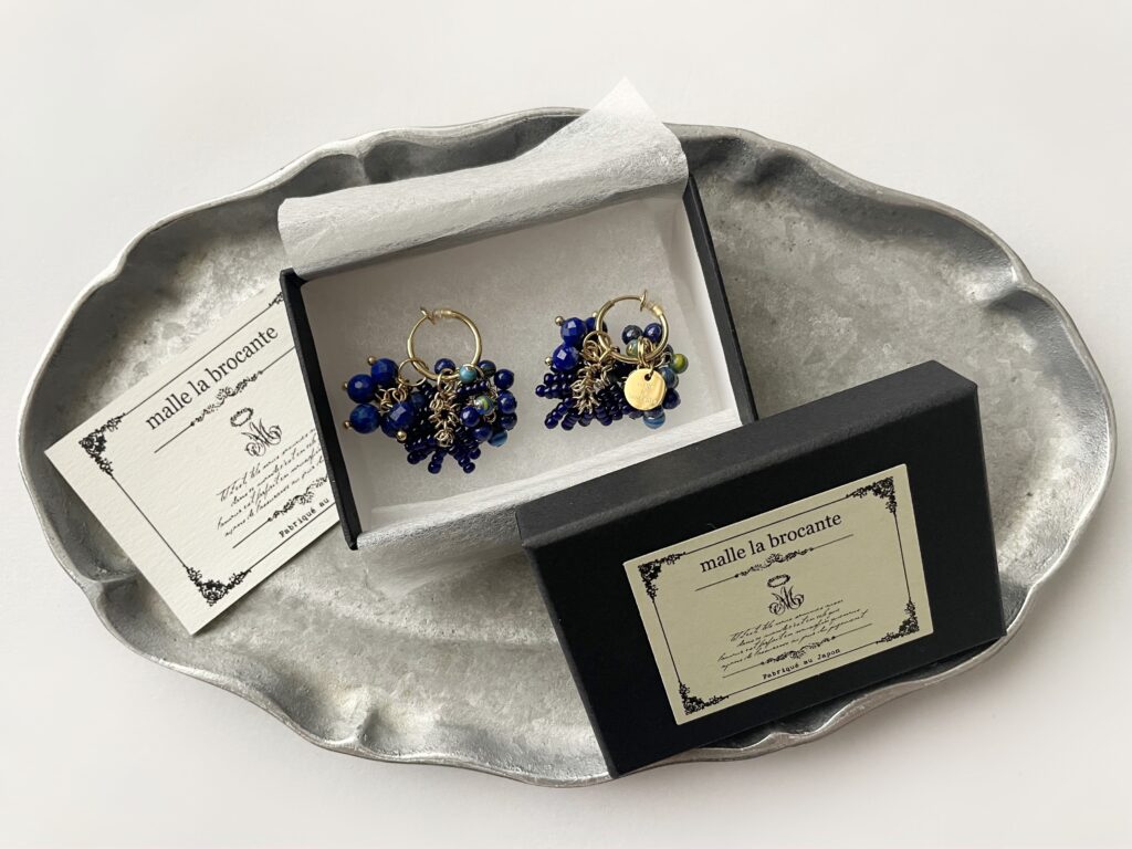 マルラブロカント（malle la brocante）のラピスラズリのイヤリング、箱に入った状態で上から撮った写真。下にシルバーのレリープレートが敷かれている。