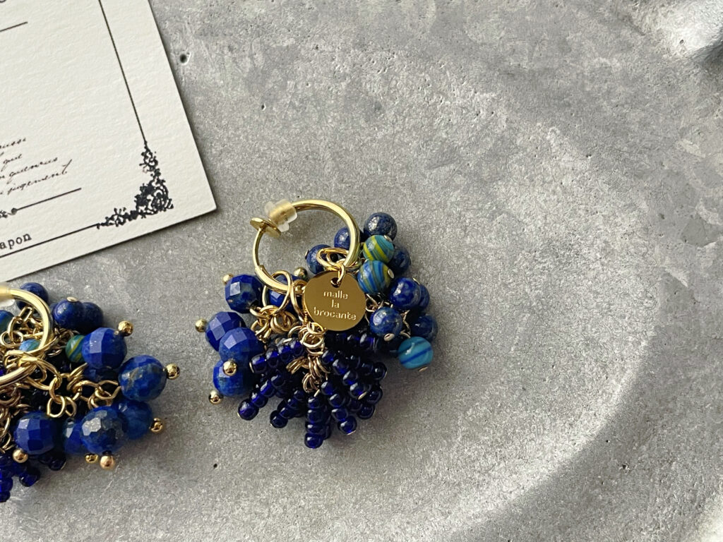 「malle la brocante」の刻印が入ったゴールドチャームがイヤリングの片耳に付いている様子