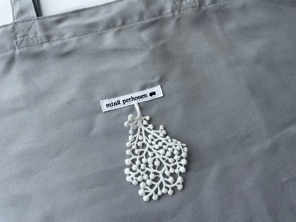 ミナペルホネンでもらえるエコバッグ。ミナペルホネンのタグに、forest paradeのレースのパーツが付いている。