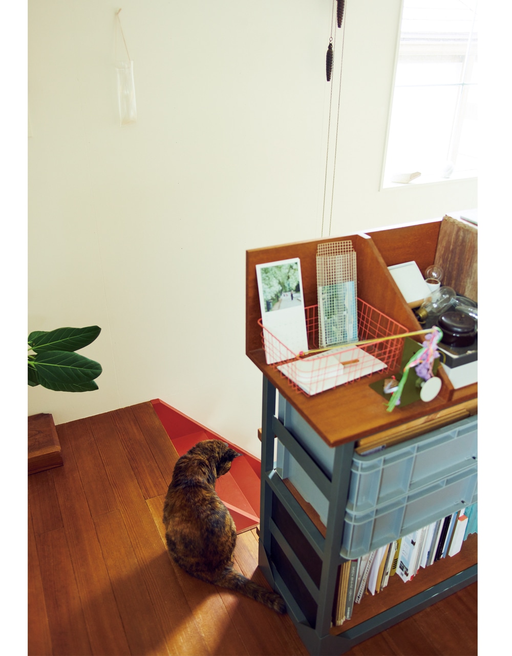 1.地上2階と半地下、3フロアで構成された戸建て。1階と2階をつなぐ階段は、最近赤く塗ったばかり。落下防止を兼ねた棚は夫の大原さんデザインで、東端さんの仕事の資料や友人の作家の作品が並ぶ。