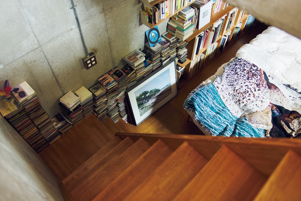 1階の玄関からすぐの、半地下の寝室へ向かう階段。本を並べた壁付けの棚は、本が増えるにつれて少しずつ増やしたもの。壁ぎわに積み上げたCDがコンクリートの壁を彩り、インテリアの一部としてなじんでいる。