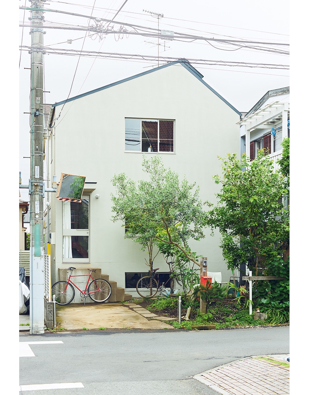 半地下があるため、1階・2階は通常より半階分高く、窓からの眺めにも開放感がある。淡いグレーの外壁が、手前の庭に植えられた木々といい相性。三角屋根もアクセントに。