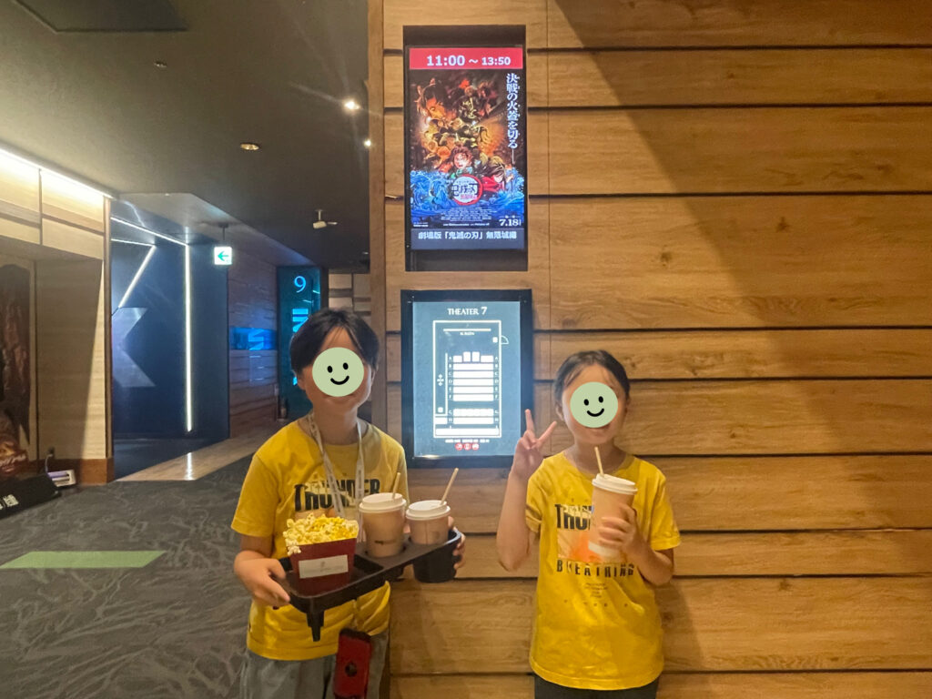 映画『劇場版 鬼滅の刃 無限城編第一章 猗窩座再来』シアター入口前で写真を撮る小学生男女。ユニクロ×鬼滅の刃コラボの善逸Tシャツをお揃いで着ている。