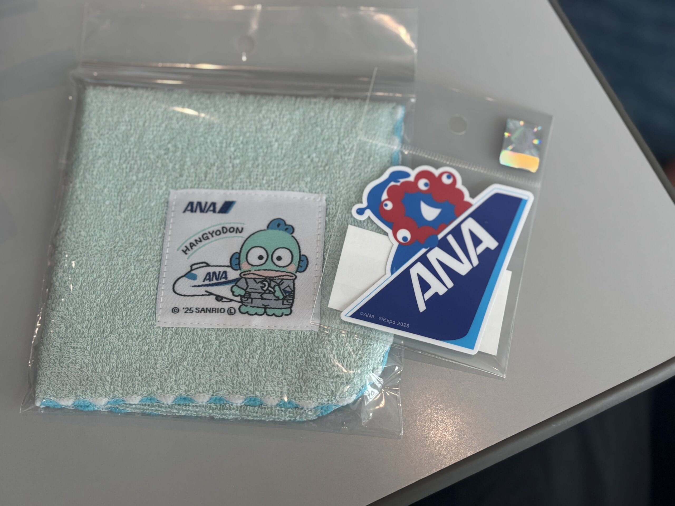 ANAとの限定コラボアイテム「ミャクミャクステッカー」（440円）、「サンリオキャラクターのハンカチ」（715円）