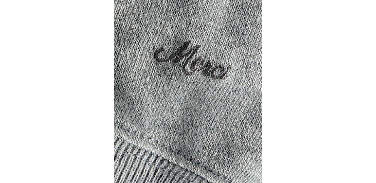 左袖口付近に生地と同系色の「Merci」のロゴ刺繍を。