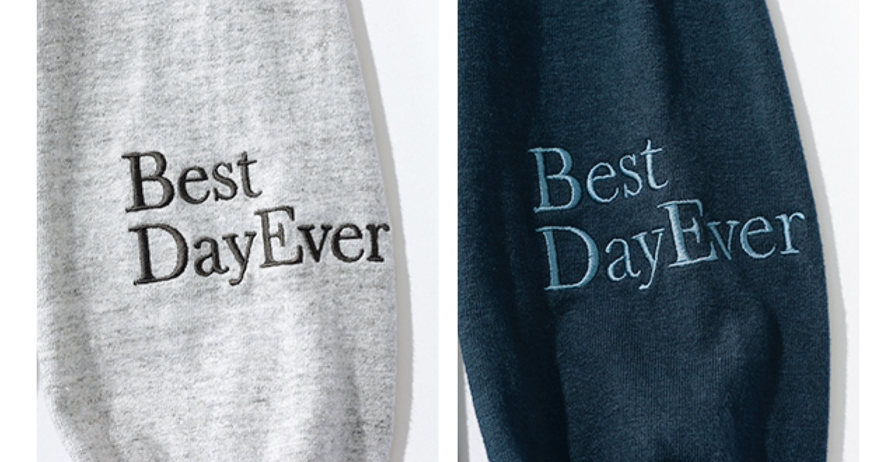 左袖に「人生最高の日！」の意味合いの英文と、 首の後ろにブランド名の刺しゅう入り。右がネイビー、左が杢グレーで、ボディと同系色。