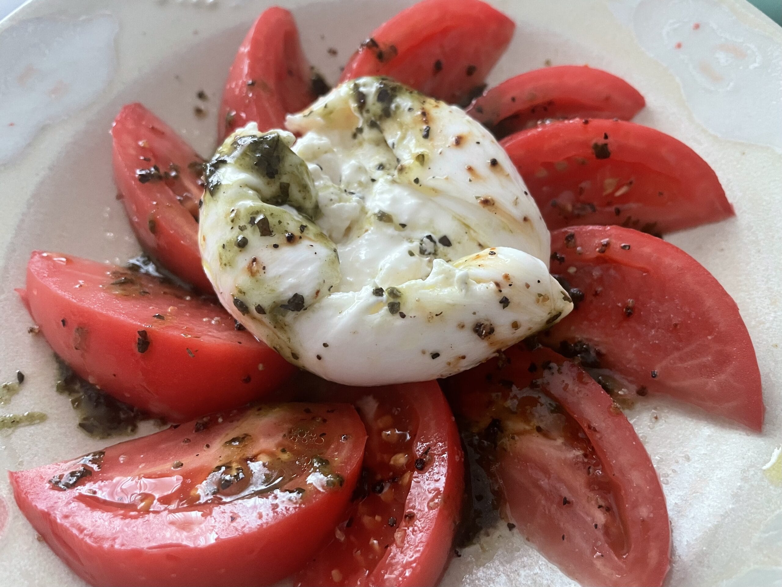 トマトのカプレーゼ、花畑牧場のブラータチーズのせ。チーズを崩してみた写真。ステーキスパイスやオリーブオイル、バジルソースがかかっている。