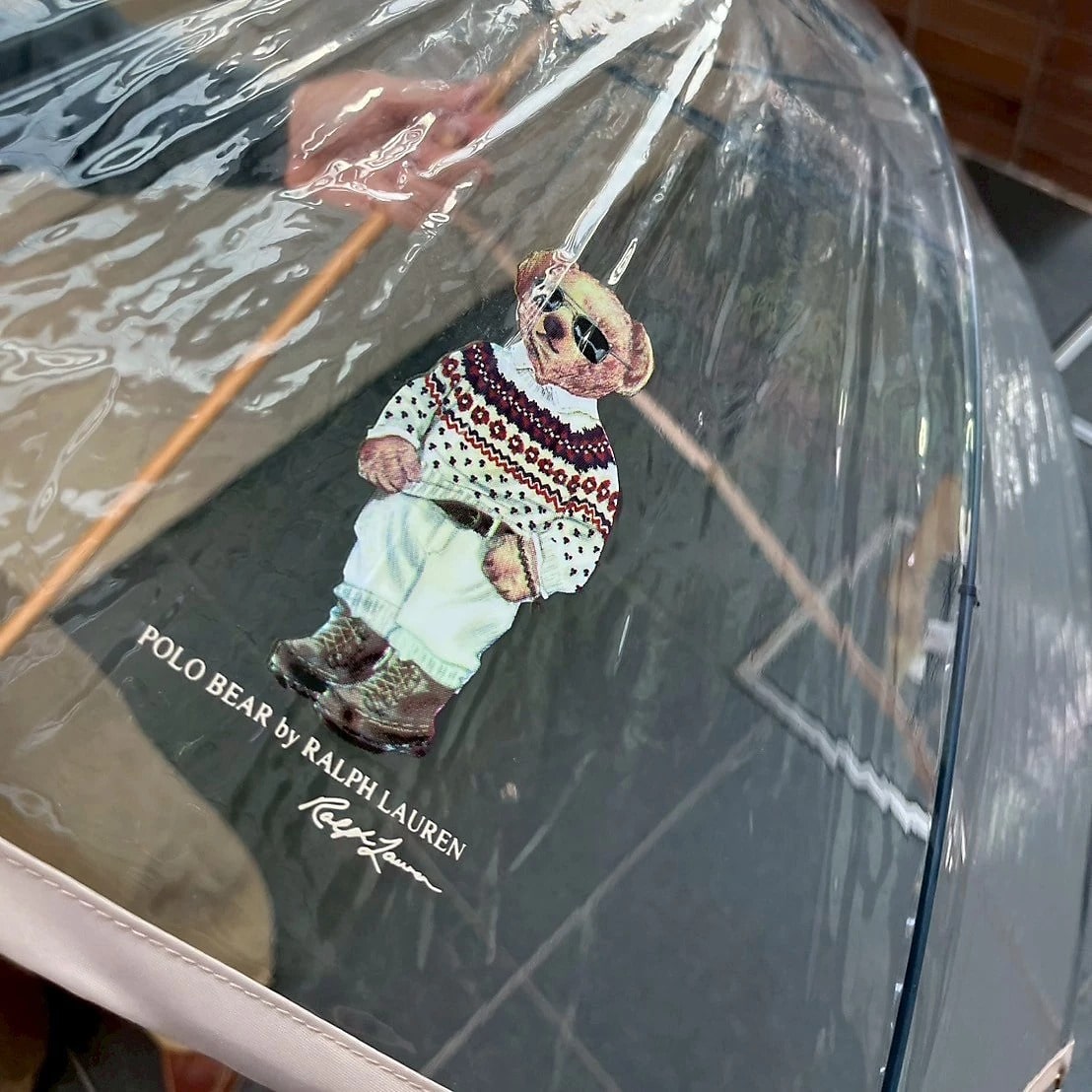 ノルディック柄のニットに白シャツをイン、ボトムスには白いパンツでサングラスをかけた洒落た冬コーデに身を包んだポロベア　ビニル傘　ベージュ