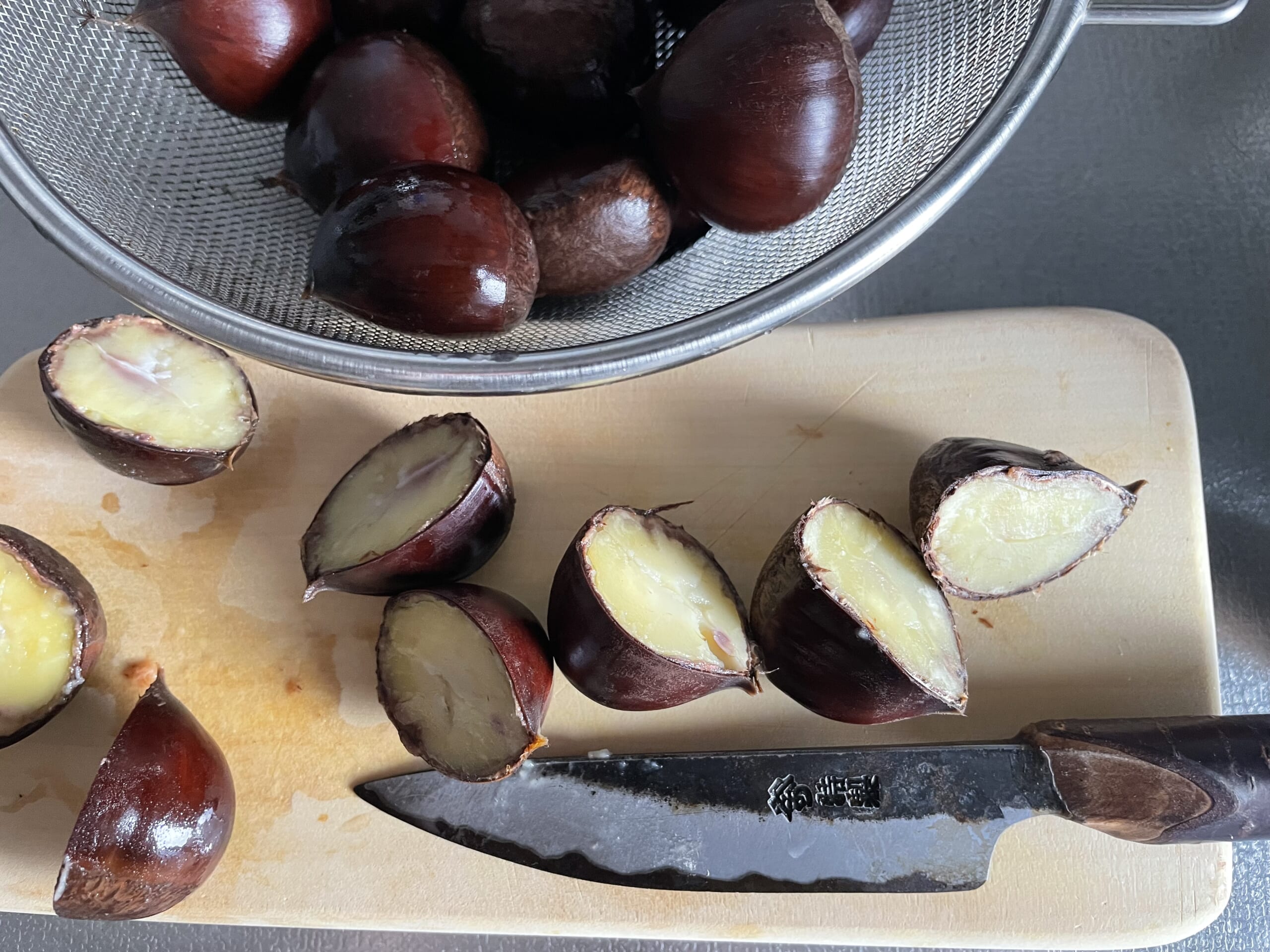 栗を鬼皮付きのまま茹でた後の写真。まな板の上で、包丁で真っ二つに切っている。