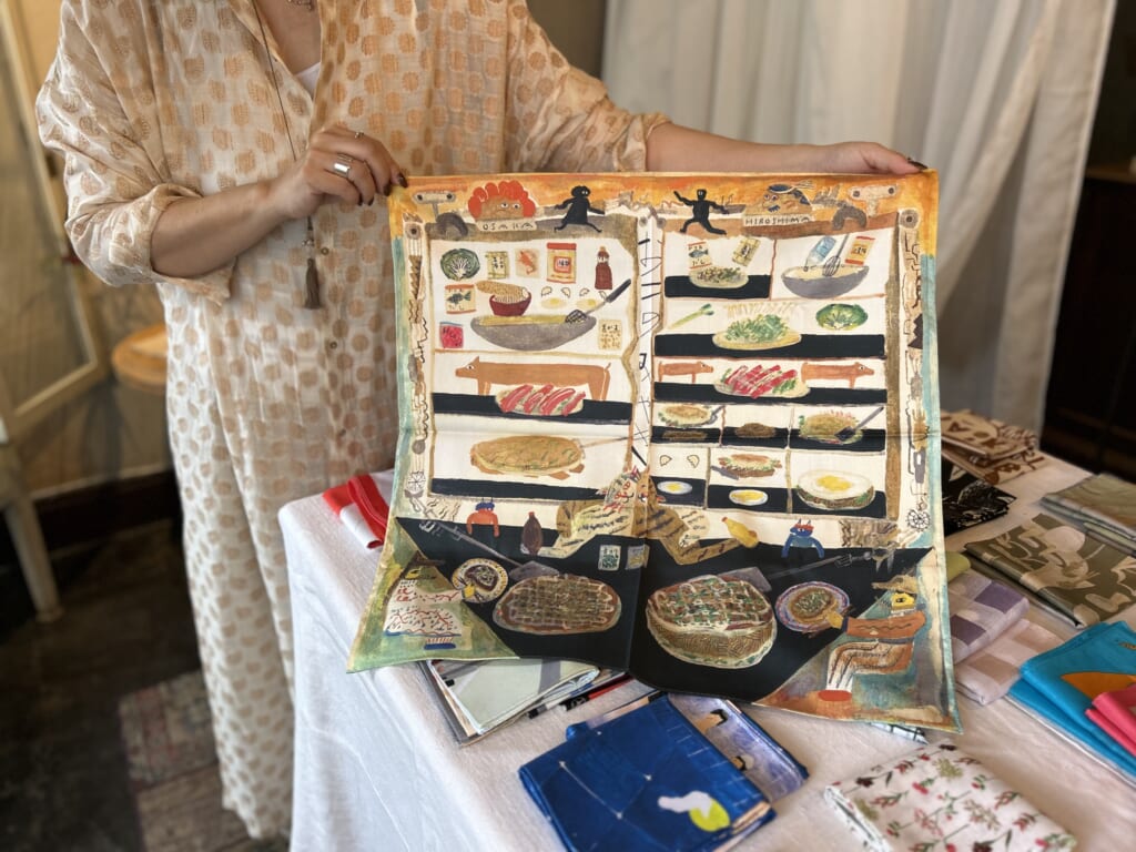 お好み焼きの柄のかわいらしいハンカチの紹介している女性。