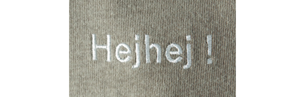 首元後ろにあしらったスウェーデン語“Hejhej！”の刺しゅうは、ベージュのボディに上品になじむ白糸を選んで、あえてさりげなく。