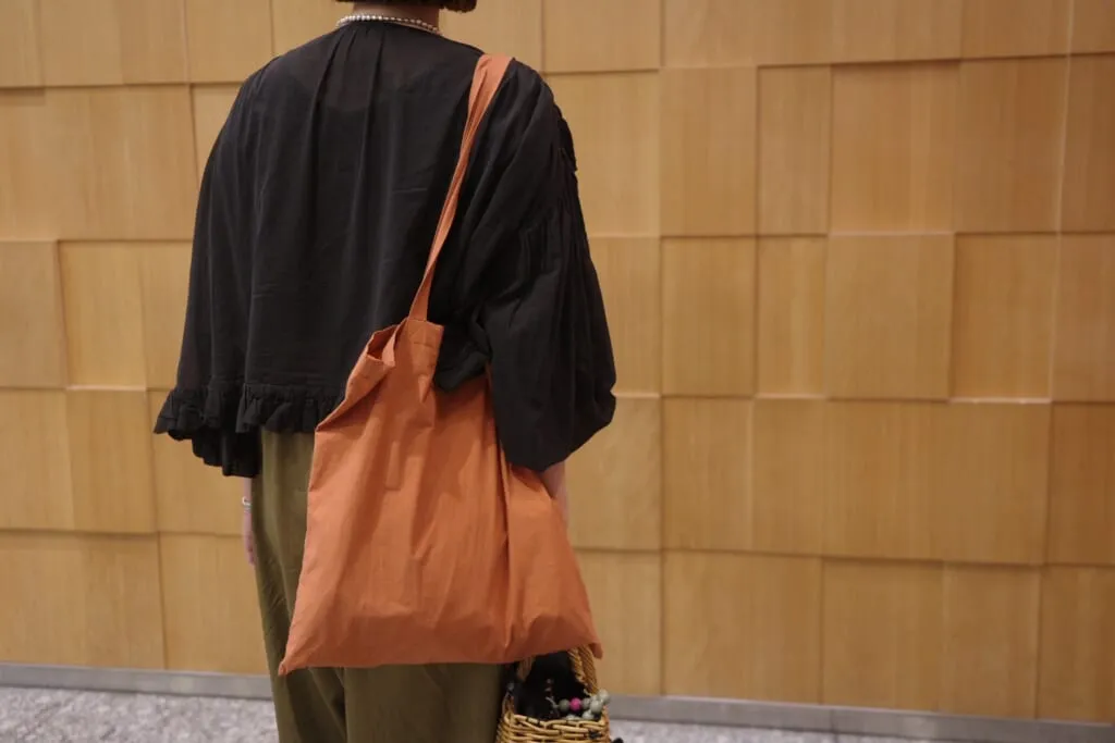 ブラウンのサブバッグを肩にかけた後ろ姿