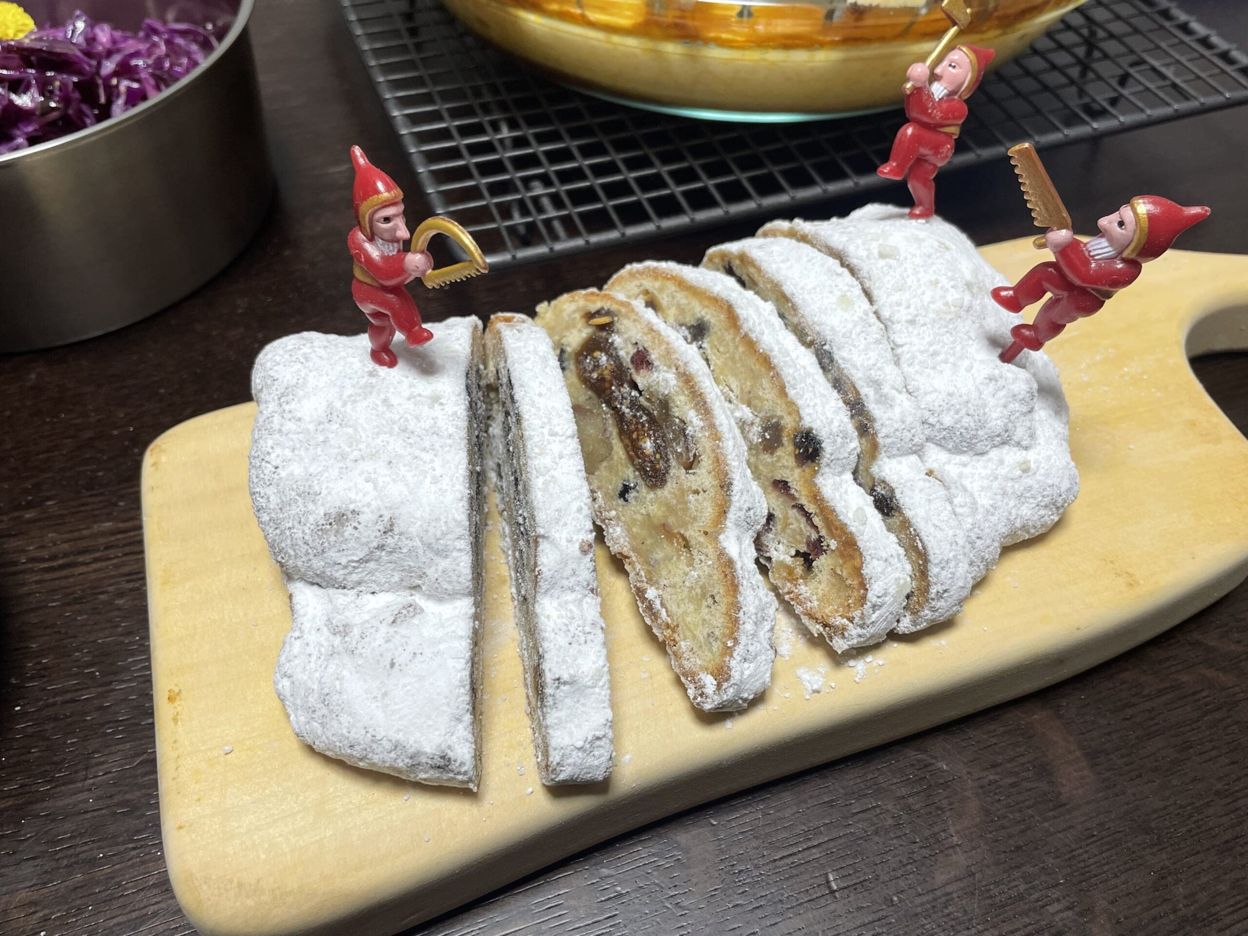 シュタットシンケン隠れ家工房のシュトーレンを薄く切ってまな板の上に並べ、森の小人ピックを3本挿した写真。