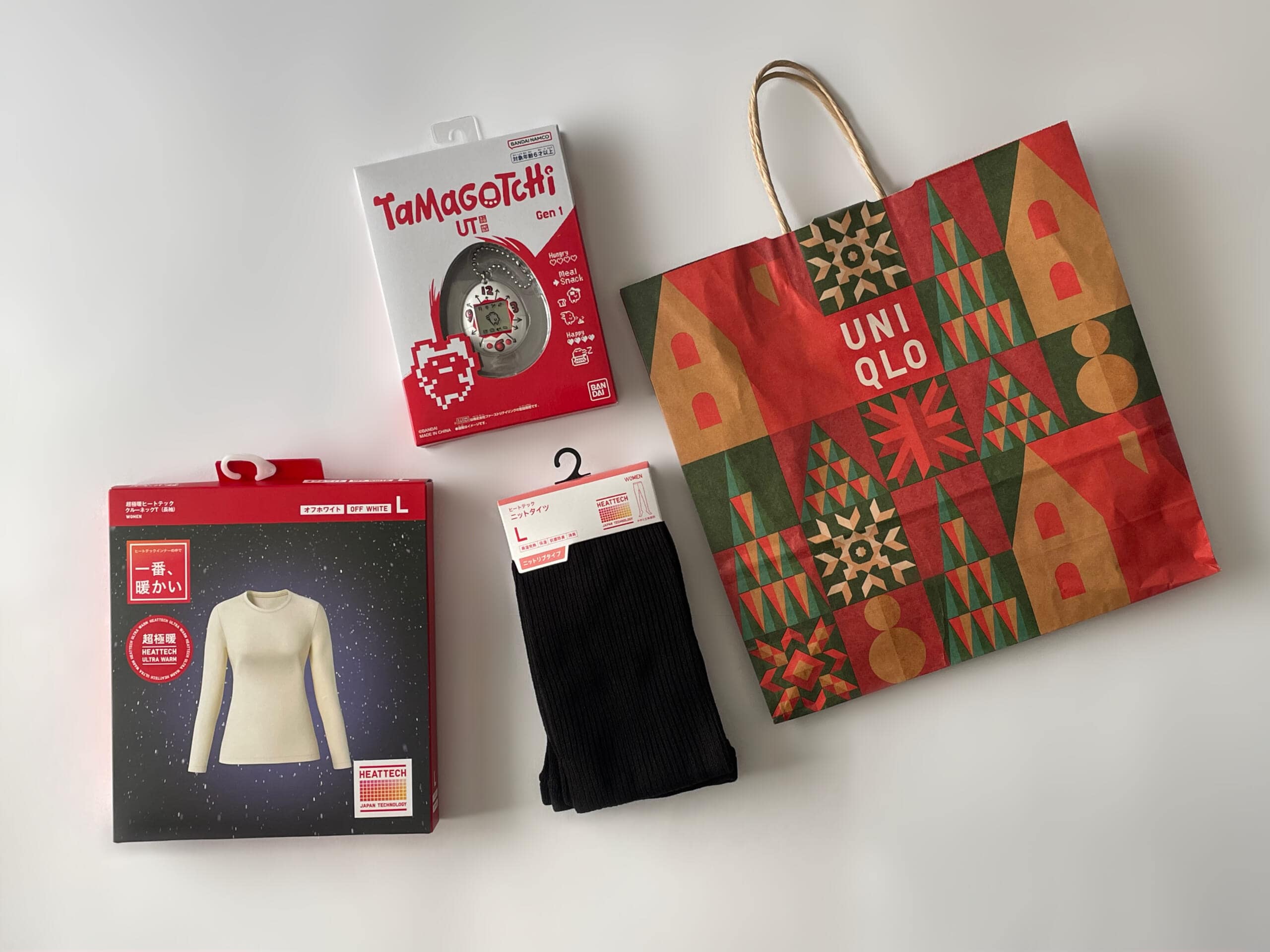 ユニクロの年末祭で買ったものを並べた写真。たまごっちやホリデーver.紙袋が並んでいる。