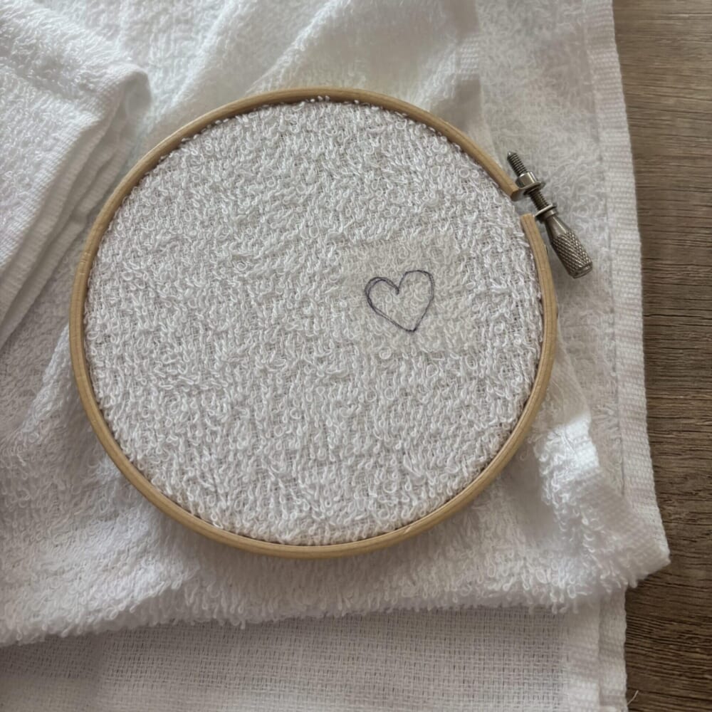 刺繍枠にはめられた、ハートの下書きの刺繍シートを貼ったフェイスタオル